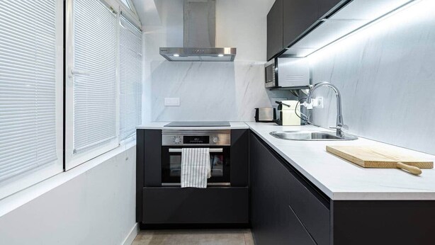 A modern kitchen with a built-in oven, a stainless steel range hood, a sink, and a wooden cutting board.