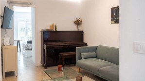Ein Wohnzimmer mit Klavier, einer Couch, einem Glastisch und einem Fernseher.