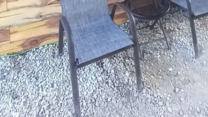 A rustic wooden wall with a metal roof, two metal chairs, and a gravel ground.
