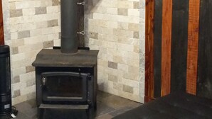 A cozy room with a black sofa, a wood-burning stove, and a brick wall.