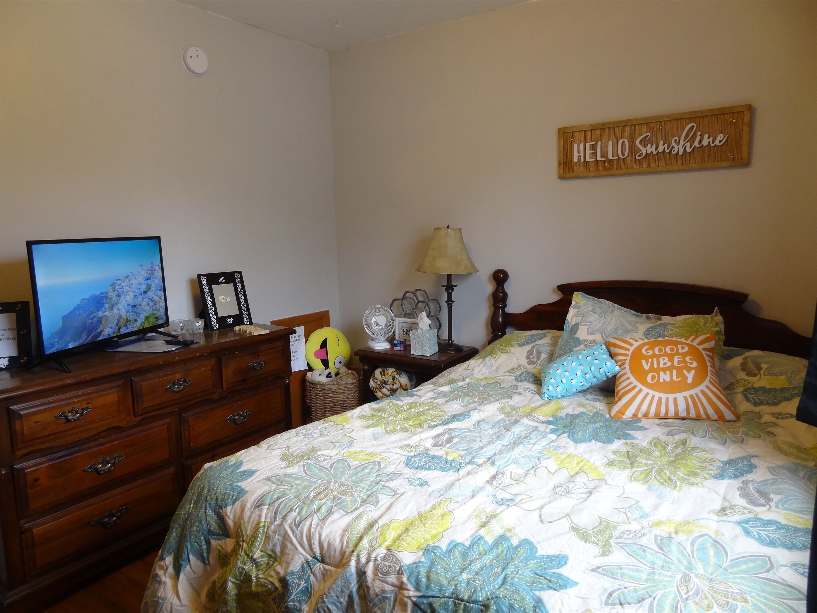 A bedroom with a bed, a dresser, a television, and a wall sign.