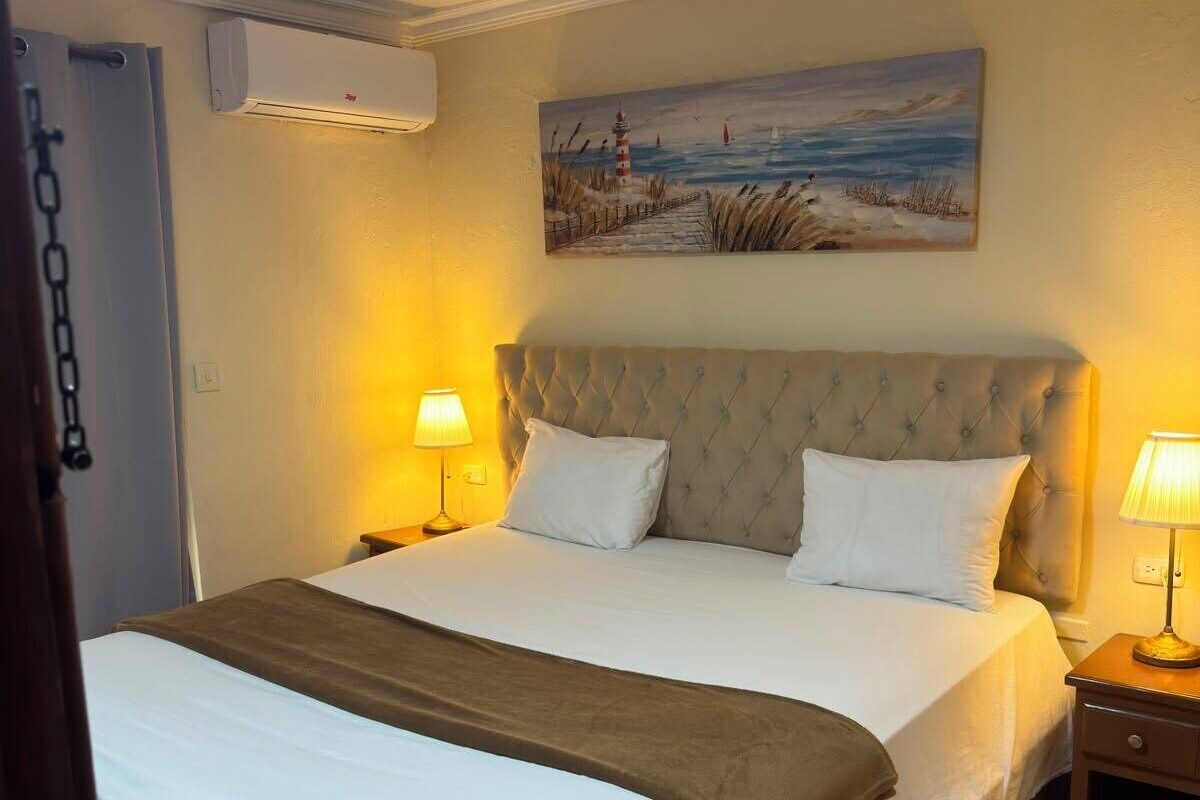 Habitación de hotel con una cama, dos lámparas de noche, un cuadro en la pared y un equipo de aire acondicionado.