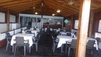 A restaurant with multiple tables and chairs, wooden ceiling beams, and ceiling fans.