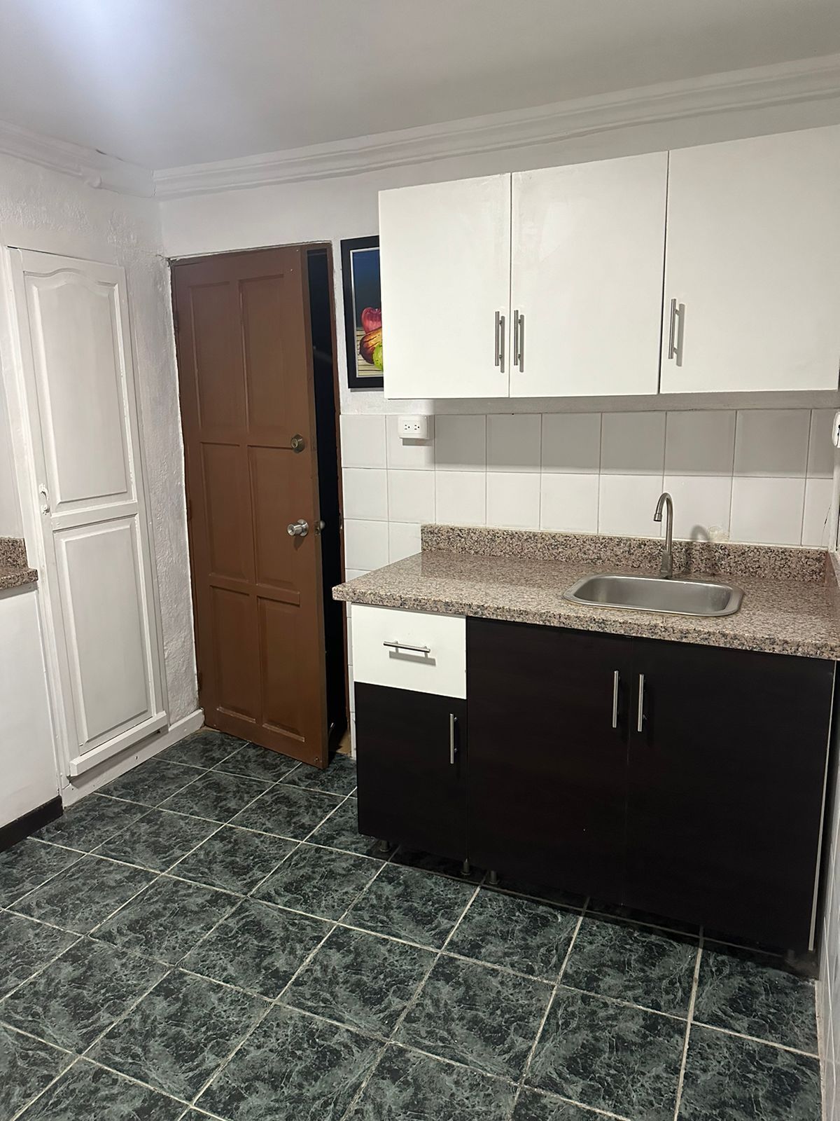 A kitchen with white cabinets, a granite countertop, a stainless steel sink, and dark tiled flooring.
