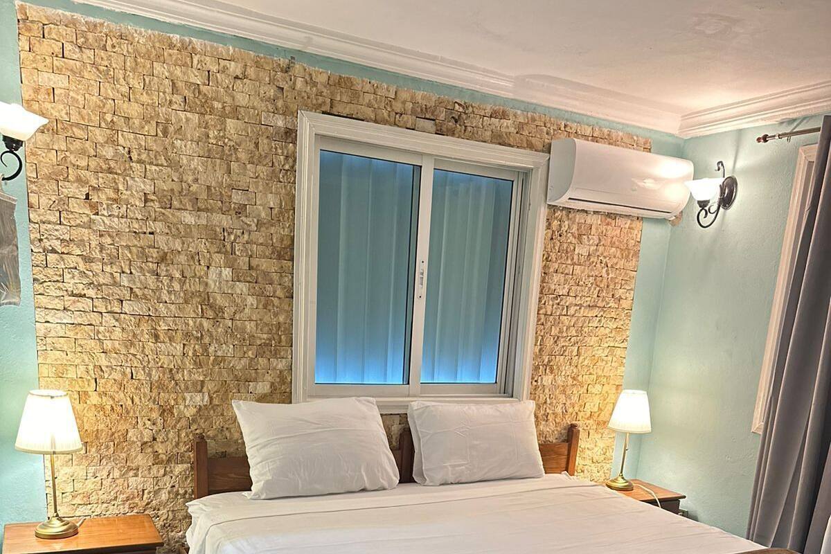 Un dormitorio con pared de piedra, una cama grande con ropa blanca, dos lámparas de noche y una ventana con cortinas.