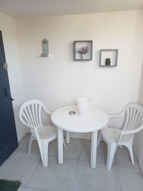 A small, round white table with two white plastic chairs, a white pitcher, and two framed pictures on the wall. - Getaway  (Fontvieille)