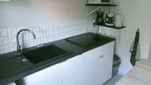 Una cocina con mostrador negro, un lavamanos, un microondas y un reloj en la pared.