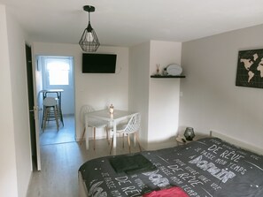 Een slaapkamer met een bed, een bureau, een stoel, een televisie en een plank met decoratieve objecten.