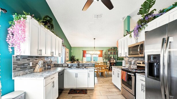 Una cocina moderna con gabinetes blancos, electrodomésticos de acero inoxidable y una pared de acento color aguamarina.