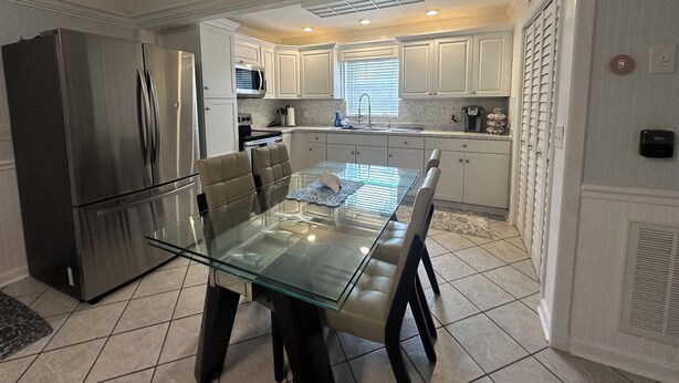 A modern kitchen with white cabinets, stainless steel appliances, and a glass dining table. - Waterfront Everglades basecamp with dock, trailer parking, and direct bay access (Ochopee)