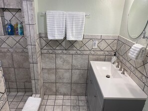 Une salle de bain avec une douche, un lavabo et un miroir. Deux serviettes blanches sont suspendues à un porte-serviettes.