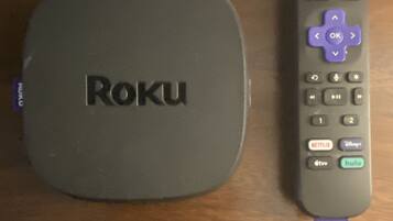 Un appareil de diffusion en continu Roku et sa télécommande, posés sur une table en bois.