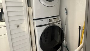 A compact laundry room with a stacked washer and dryer, a mop, and visible plumbing. - Waterfront Everglades basecamp with dock, trailer parking, and direct bay access (Ochopee)