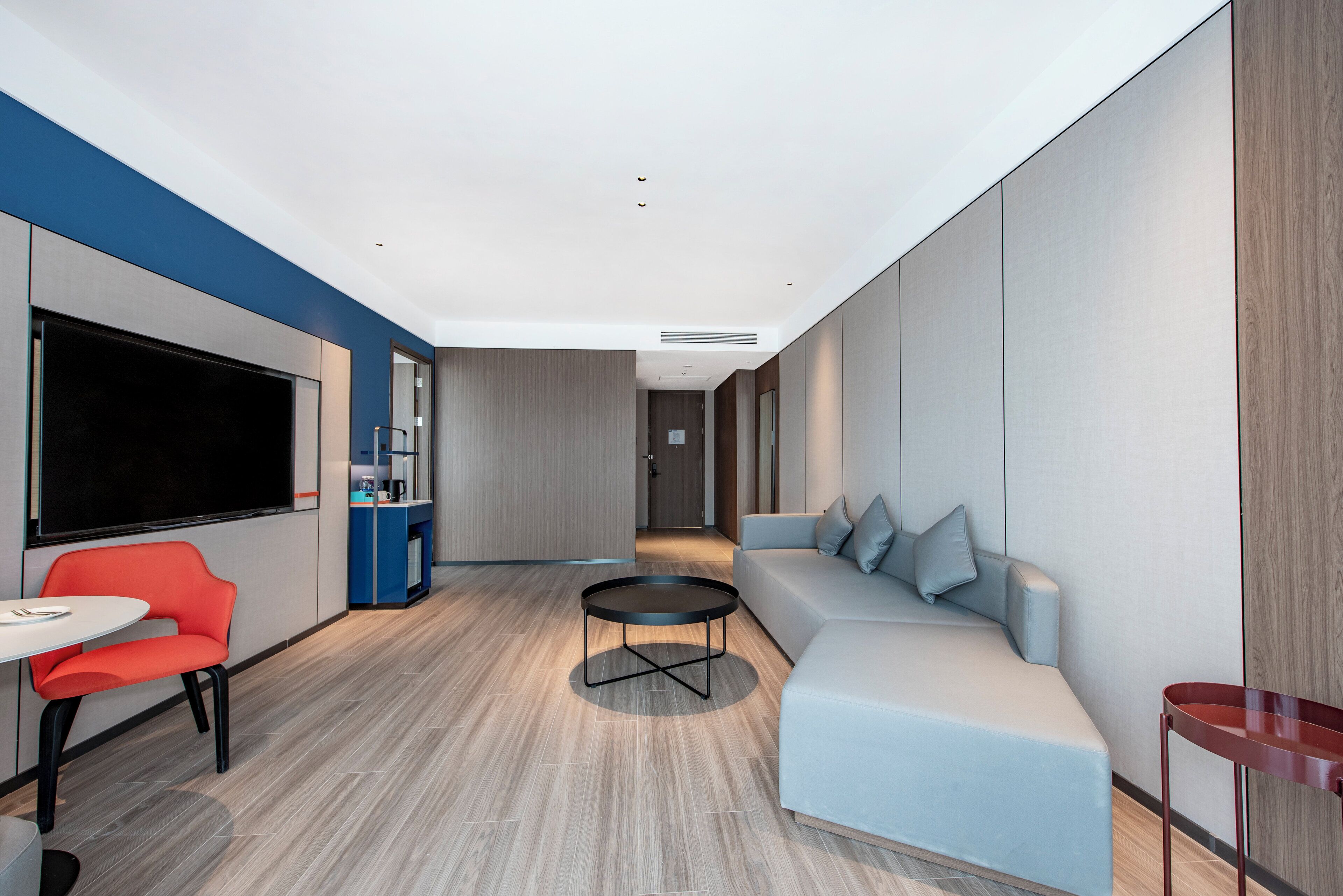 Une chambre d’hôtel moderne dotée d’un grand téléviseur à écran plat, d’une table basse ronde, d’un canapé et d’un fauteuil rouge.