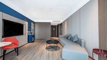 Habitación de hotel moderna con un televisor de pantalla plana grande, una mesa redonda para café, un sofá y una silla roja.