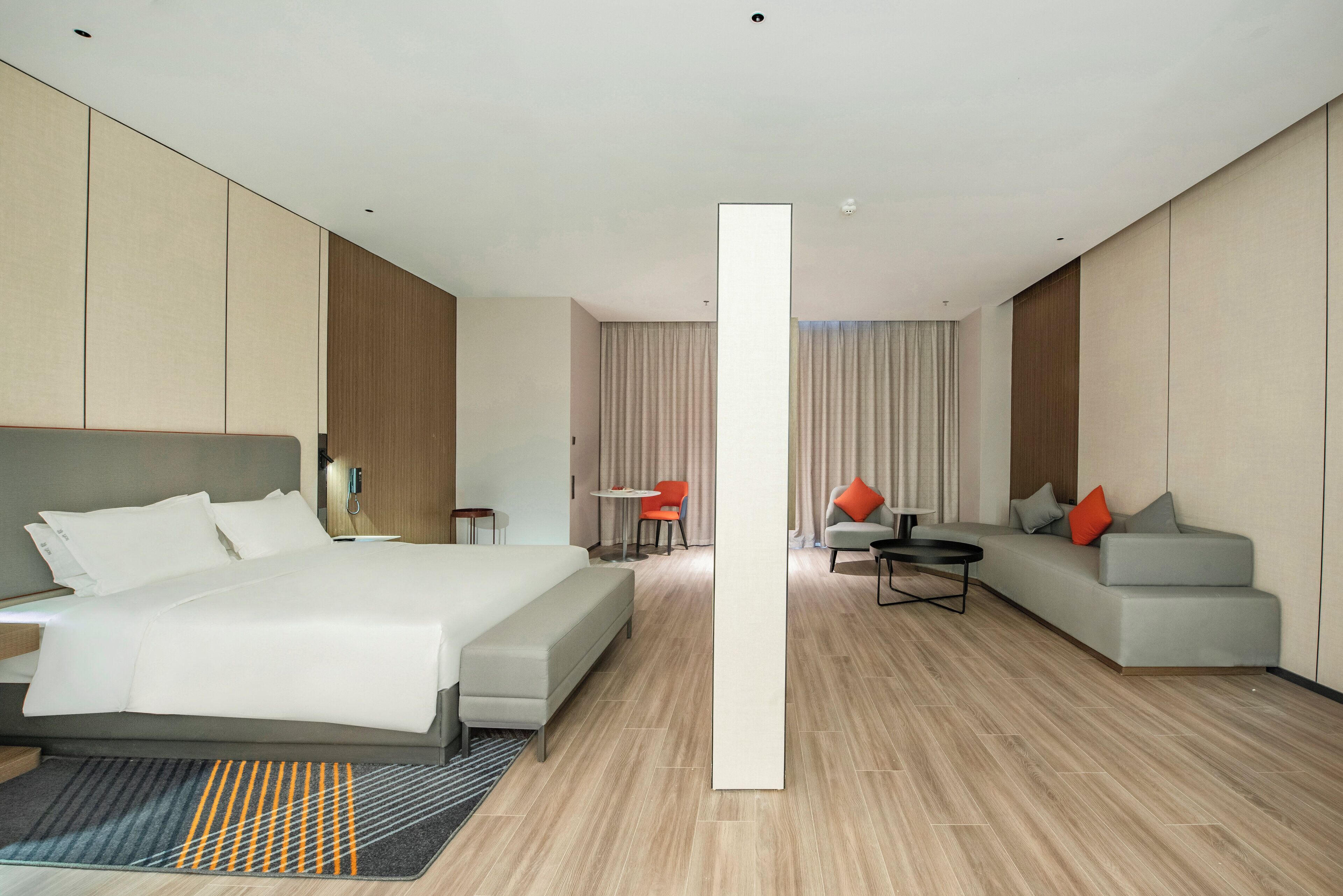 A modern hotel room with a large bed, a sofa, a coffee table, and a small table with a chair.