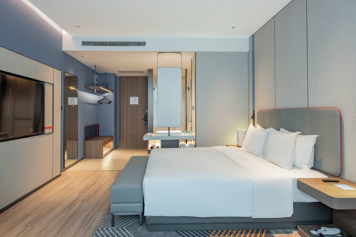 Una moderna camera d'albergo con un letto grande, una TV, uno specchio, un lavabo e una panca.