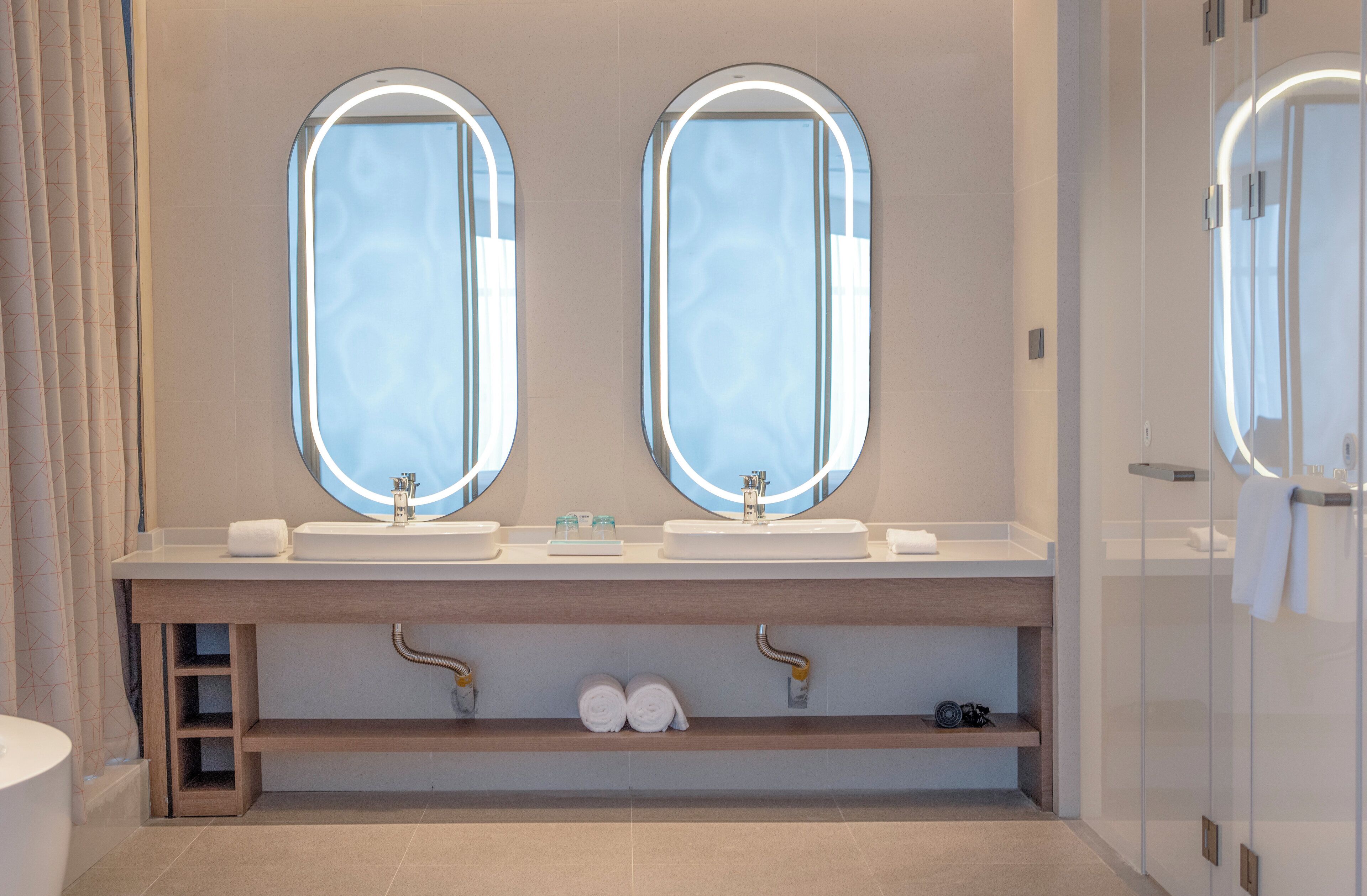 Un baño moderno con dos lavamanos, un espejo grande y una cabina de ducha con mampara de cristal.