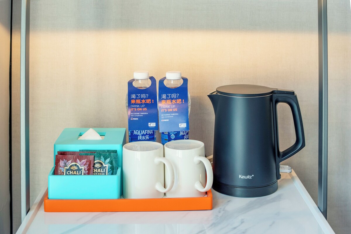 A tray with two white mugs, two cartons of Aquafina water, a Keurig coffee maker, and a tissue box with Chali tea bags.