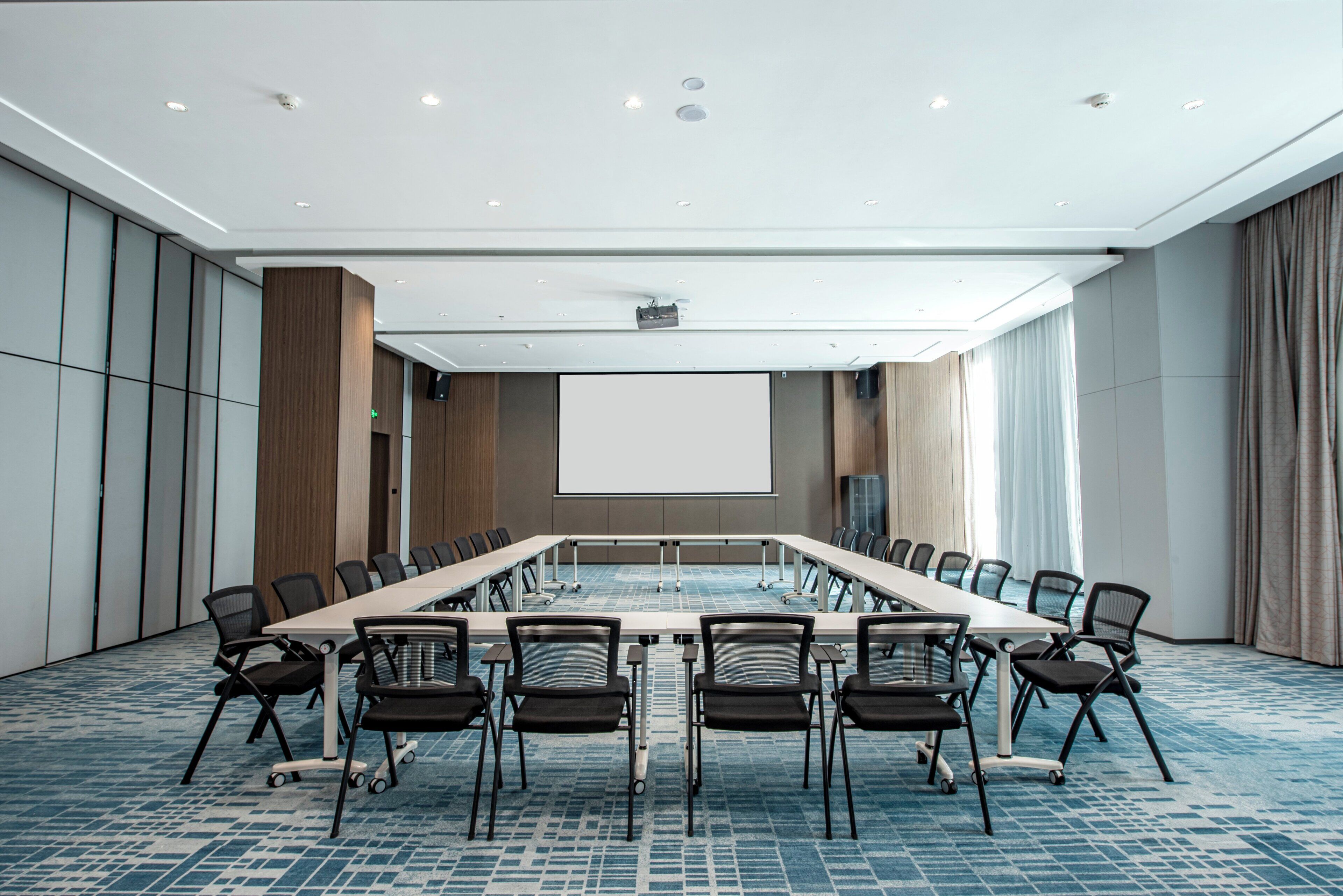 A conference room with a long table, chairs, a projector screen, and a carpeted floor.