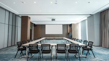 A conference room with a long table, chairs, a projector screen, and a carpeted floor.