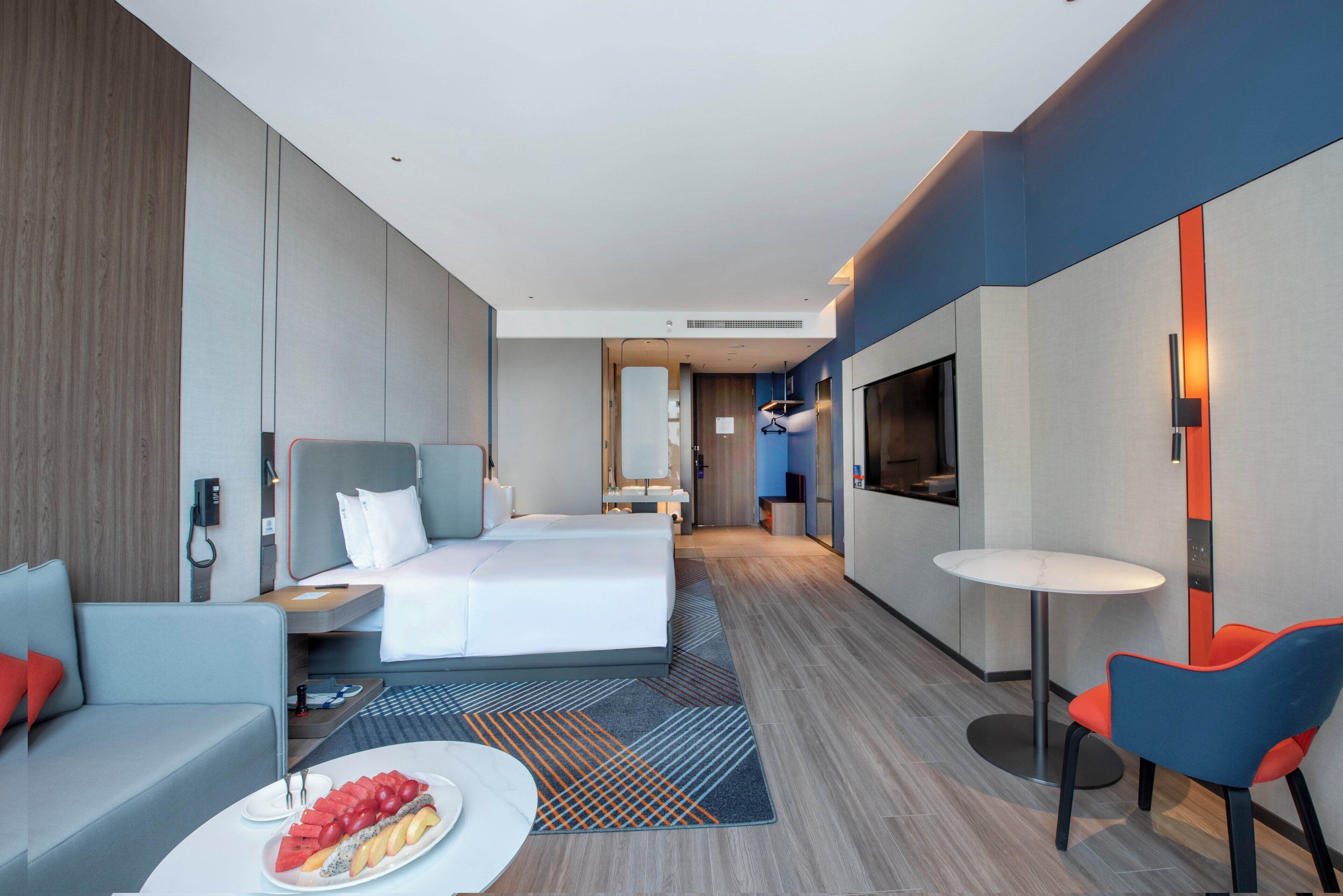 A modern hotel room with a bed, a sofa, a dining table, and a TV.