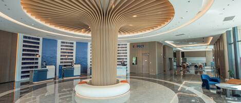 Un moderno vestíbulo de hotel con una zona de estar circular central, una recepción y una gran columna de madera.