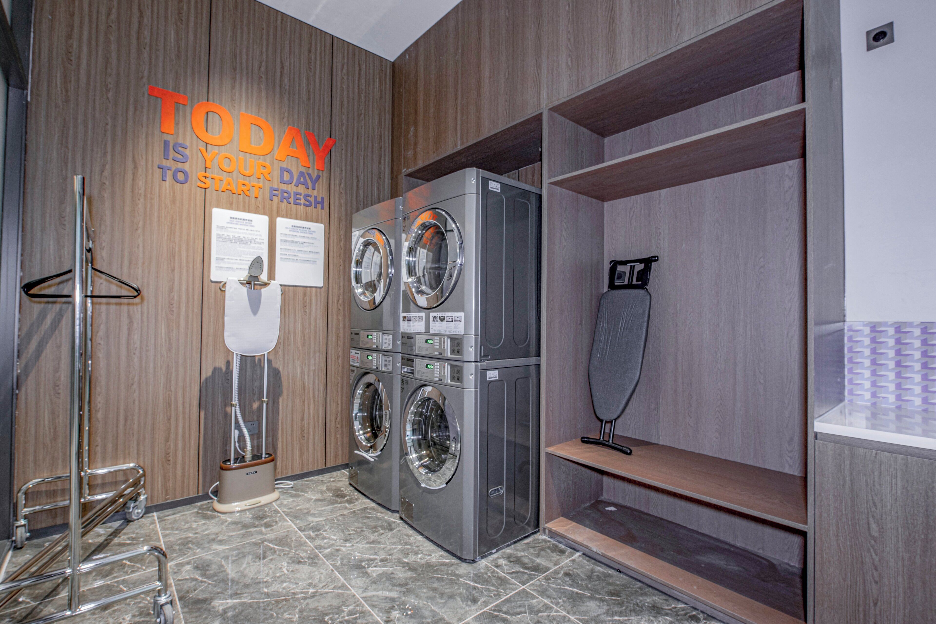 A modern laundry room with two front-loading washing machines, a wall-mounted toilet paper dispenser, and a metal cart.