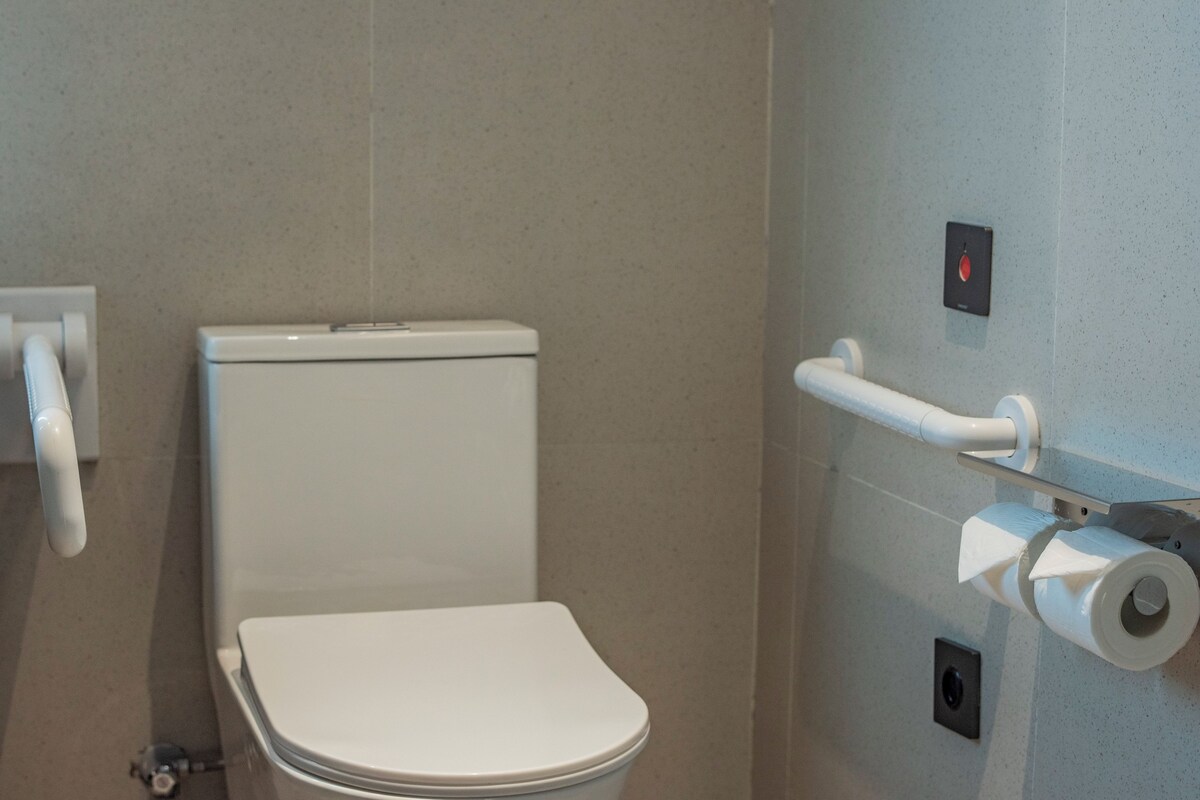 A modern bathroom with a white toilet, a hand dryer, and a paper towel dispenser.