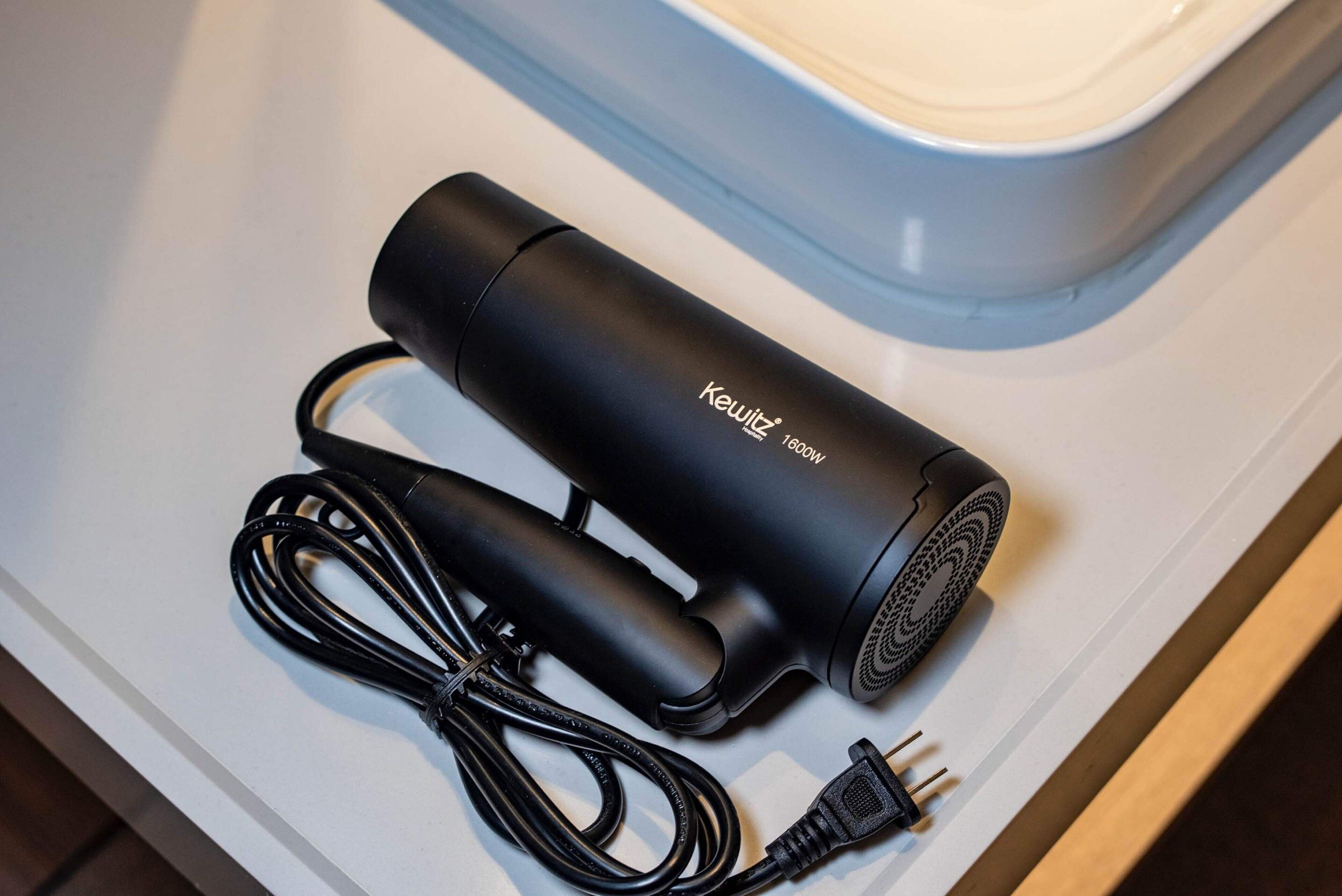 Un purificador de aire portátil negro con cable y adaptador de corriente sobre una superficie blanca.