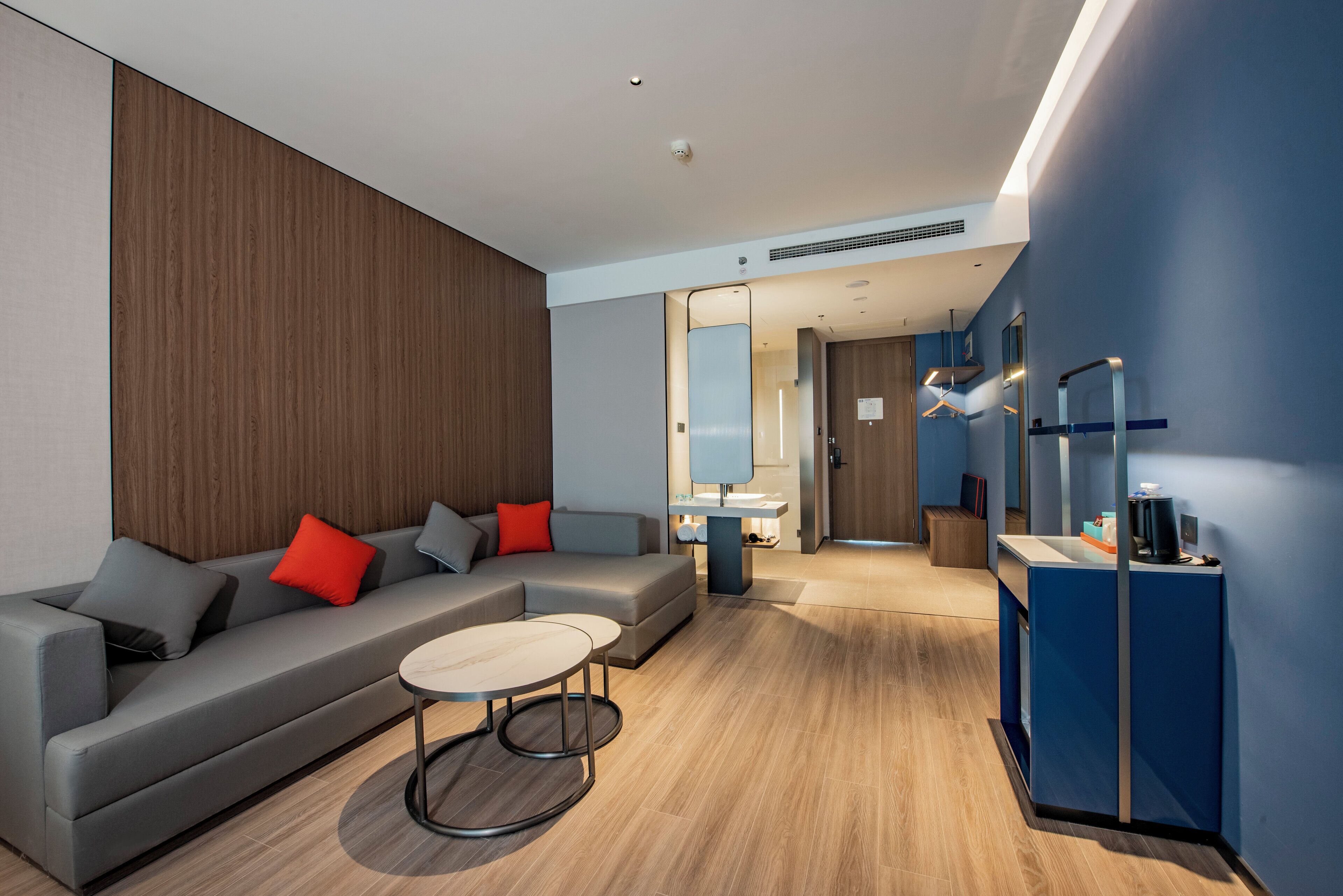 Une chambre d’hôtel moderne avec un canapé gris, une table basse ronde et un mur d’accent bleu.