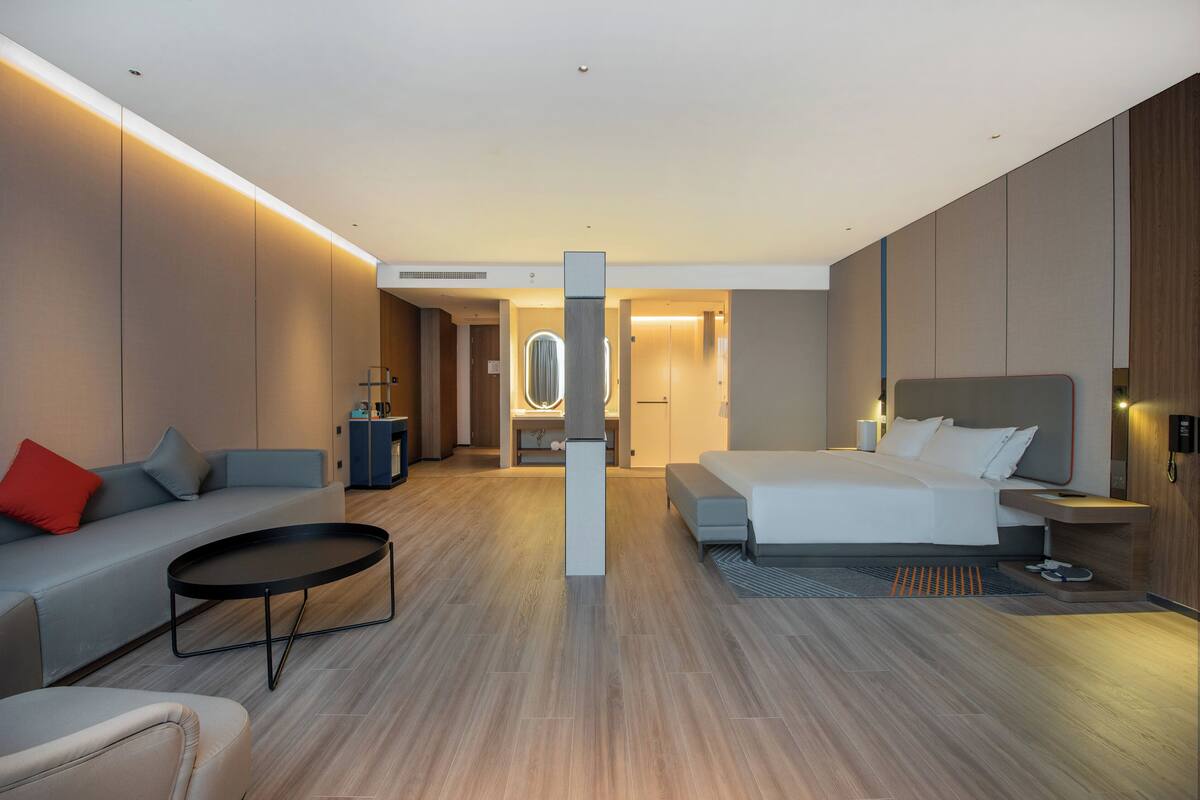 Una camera d'albergo moderna con un divano, un letto, un tavolino e un bagno sullo sfondo.