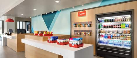 Un espace d’accueil moderne comprenant un comptoir, un réfrigérateur rempli de boissons et un mur où sont exposés divers produits d’épicerie.