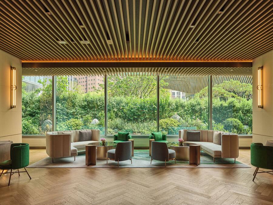 Un hall d’entrée moderne avec un plafond en bois, de grandes fenêtres et un espace détente comprenant des canapés et des fauteuils.
