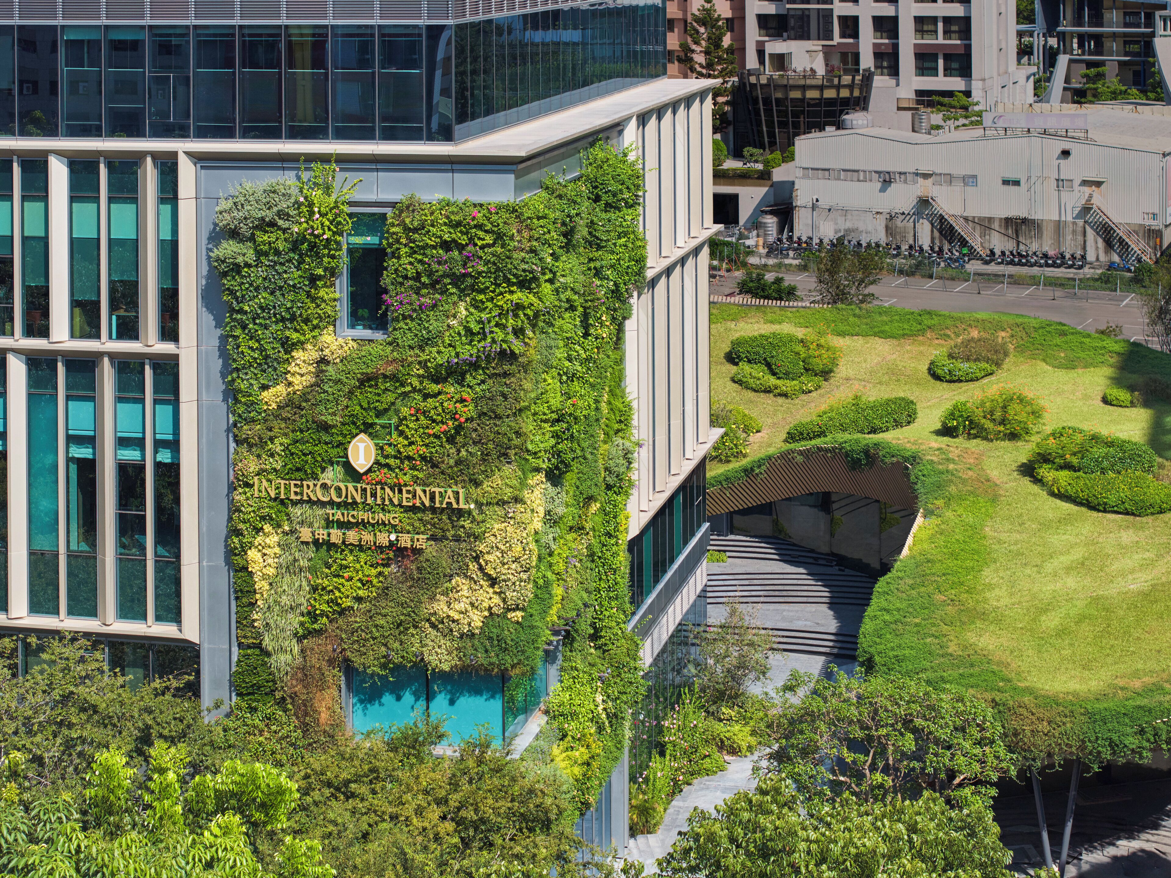 Un edificio moderno con fachada de jardín vertical, un cartel que indica 'INTERCONTINENTAL TAICHUNG' y un césped bien cuidado con senderos.