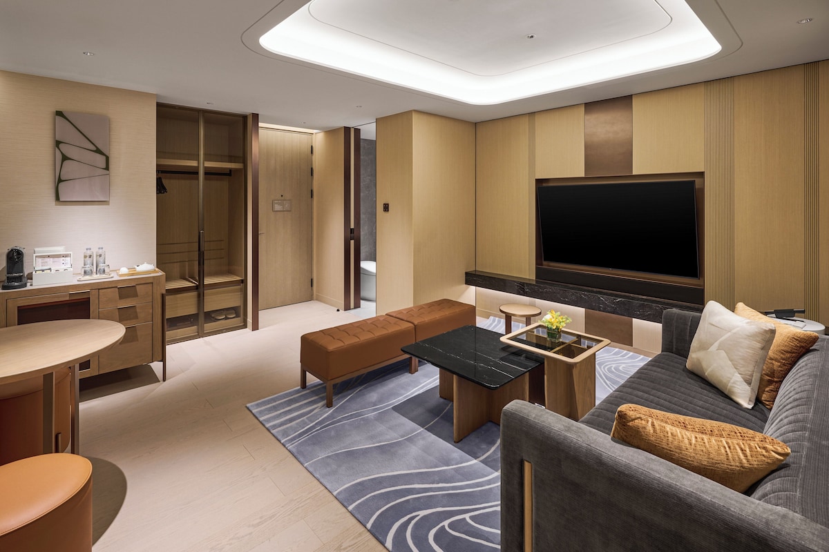 Une chambre d’hôtel moderne équipée d’un canapé, d’une table basse, d’une télévision, d’un bureau et d’une salle de bain.