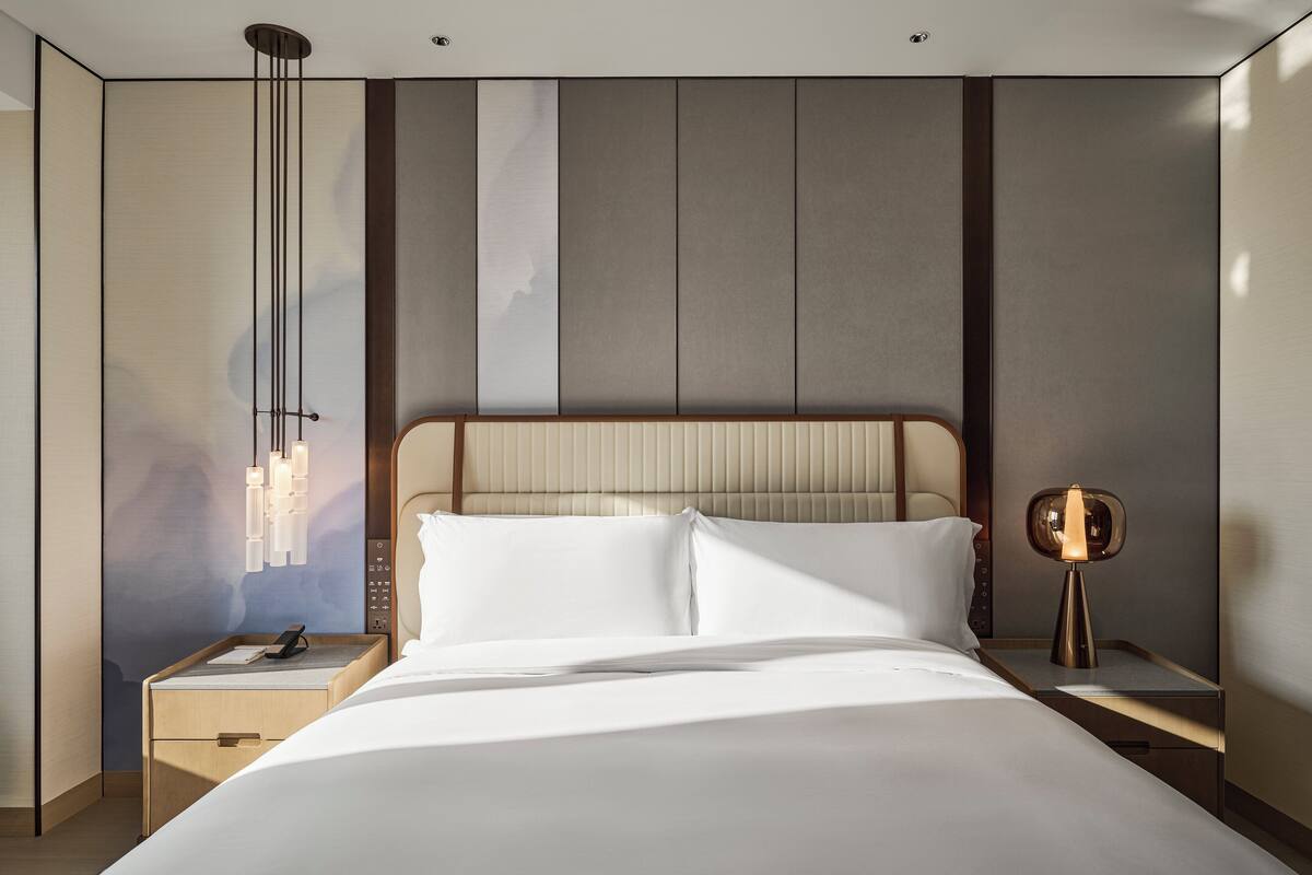Una habitación de hotel moderna con una cama grande, una mesita de noche con lámpara y un aparador con teléfono.
