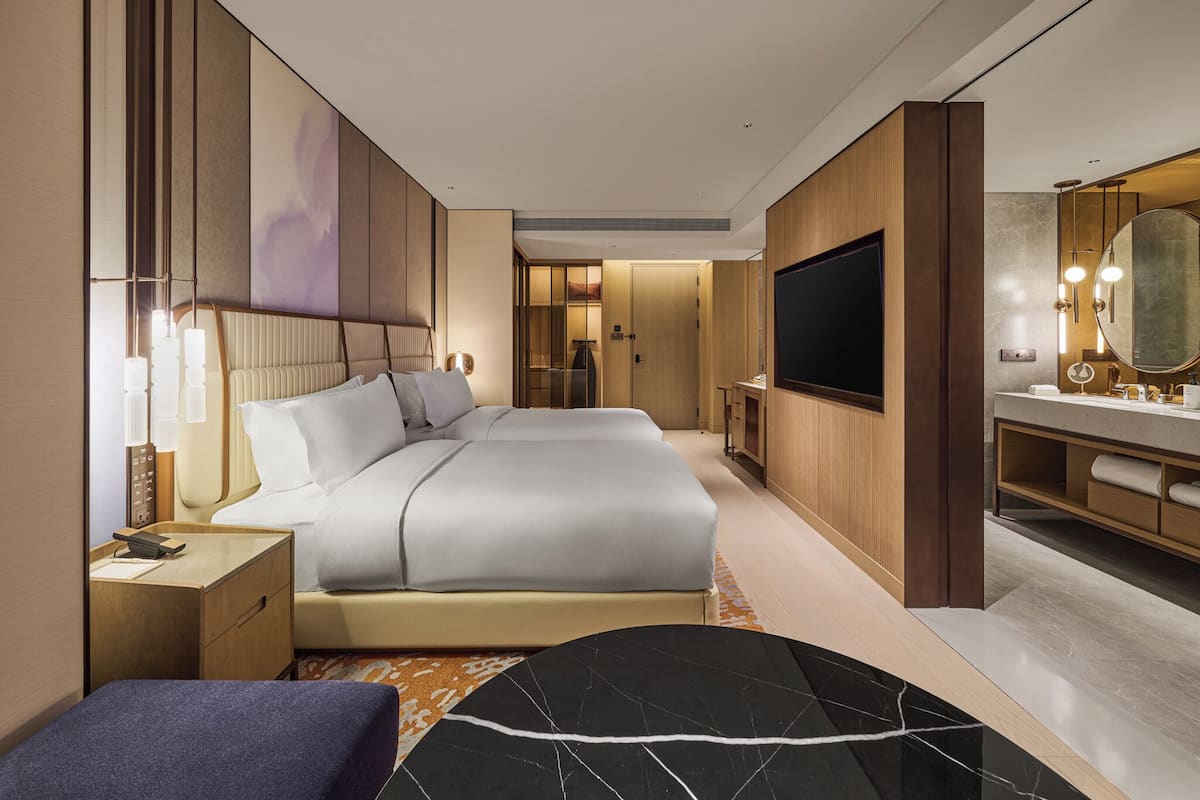 Una habitación de hotel moderna con una cama grande, televisión, escritorio y baño con espejo y lavamanos.