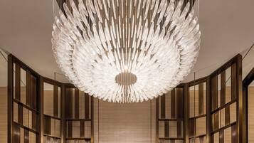 A modern hotel lobby with a central chandelier, mirrored walls, and a geometric floor pattern.