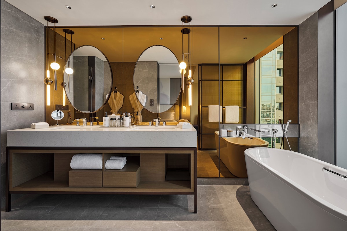 Une salle de bain moderne dotée d’un grand meuble-lavabo, de deux miroirs et d’une baignoire sur pieds.
