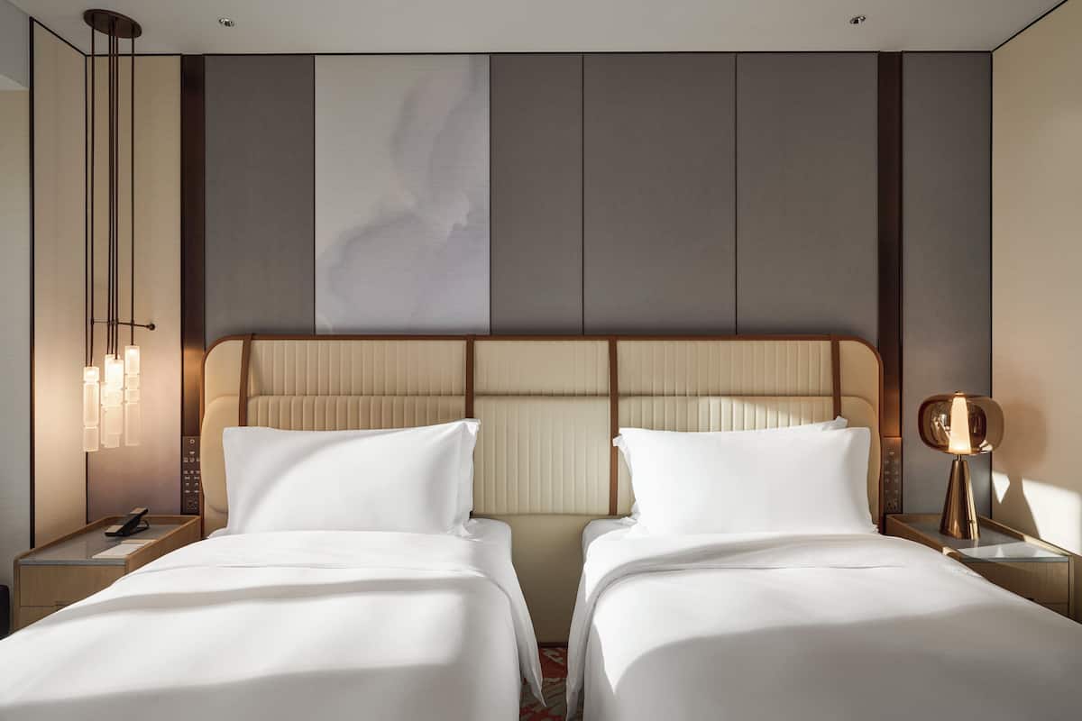 Una habitación de hotel con dos camas, una obra de arte grande en la pared y una lámpara moderna.