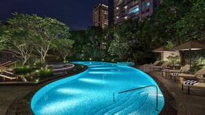 A swimming pool with a curved design, surrounded by lounge chairs and umbrellas, set against a backdrop of trees and high-rise buildings. - Intercontinental Taichung by IHG (Taichung)
