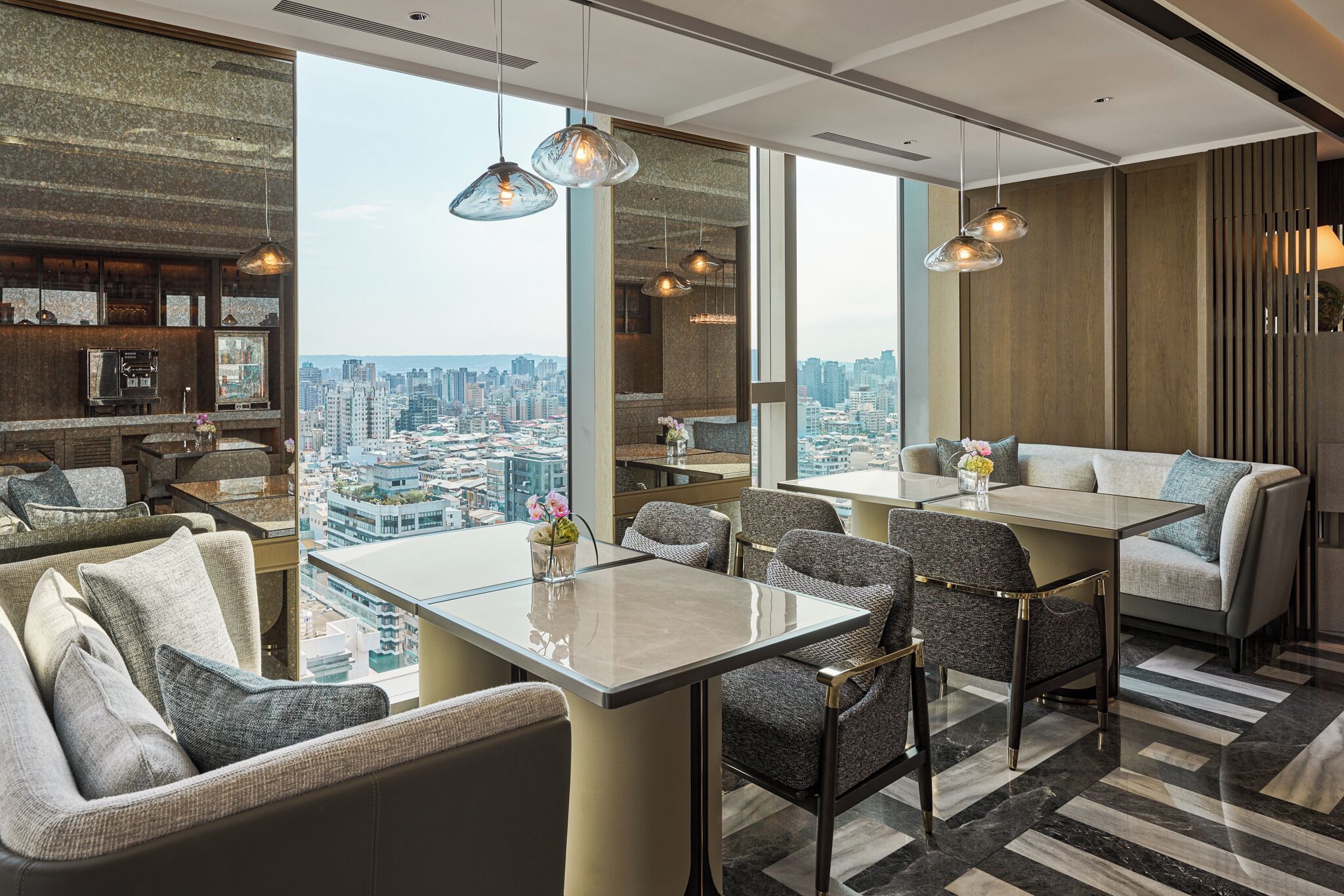 A modern hotel room with a city view, a dining area with a glass table, and a cozy seating area with sofas and chairs.