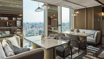 A modern hotel room with a city view, a dining area with a glass table, and a cozy seating area with sofas and chairs.