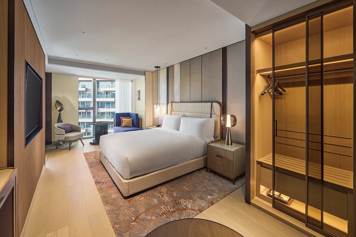 Una habitación de hotel moderna con una cama grande, mesitas de noche, un armario y vistas a la ciudad.