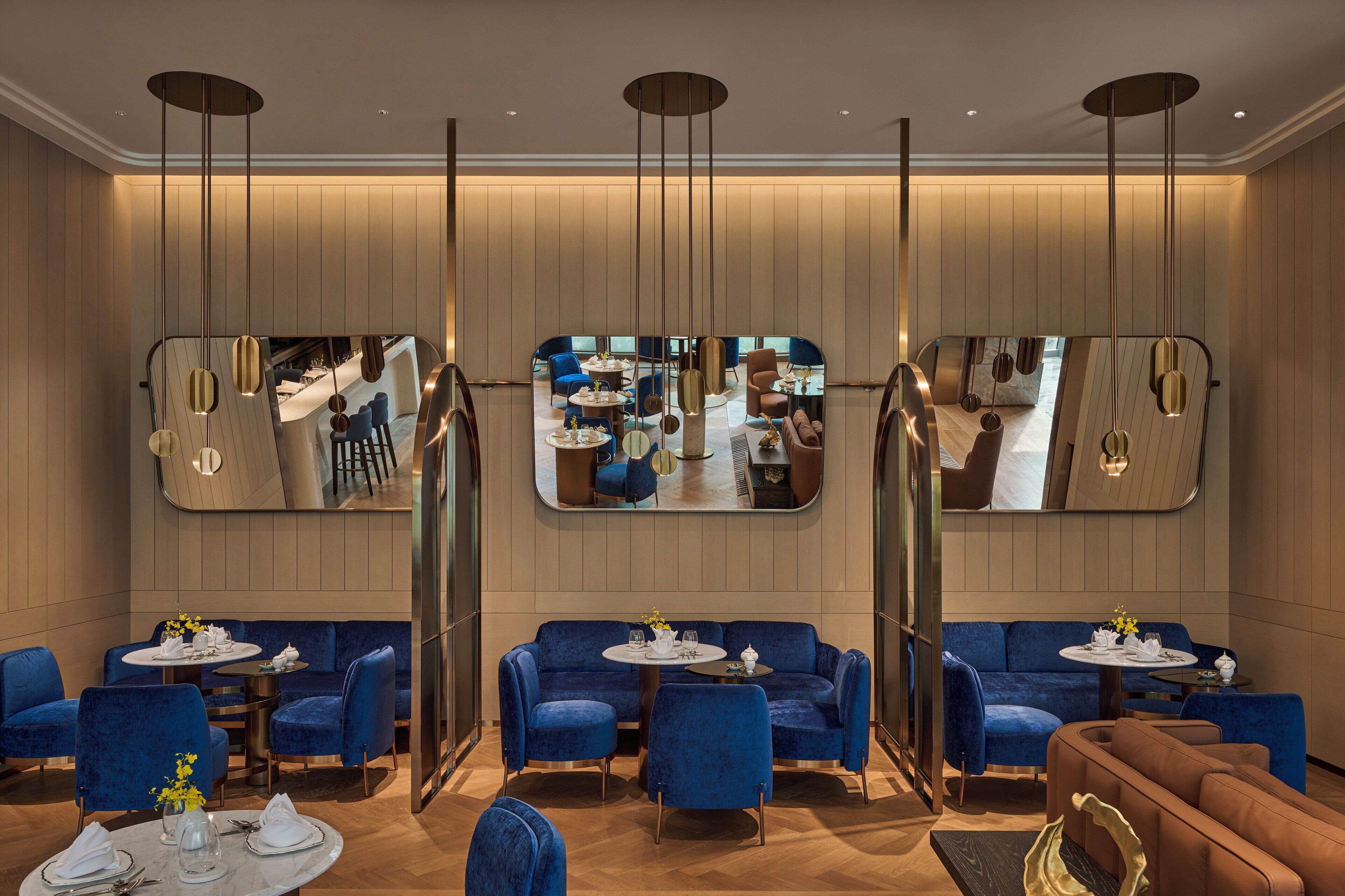 A modern hotel lobby with blue seating, a central mirror, and a wooden floor.