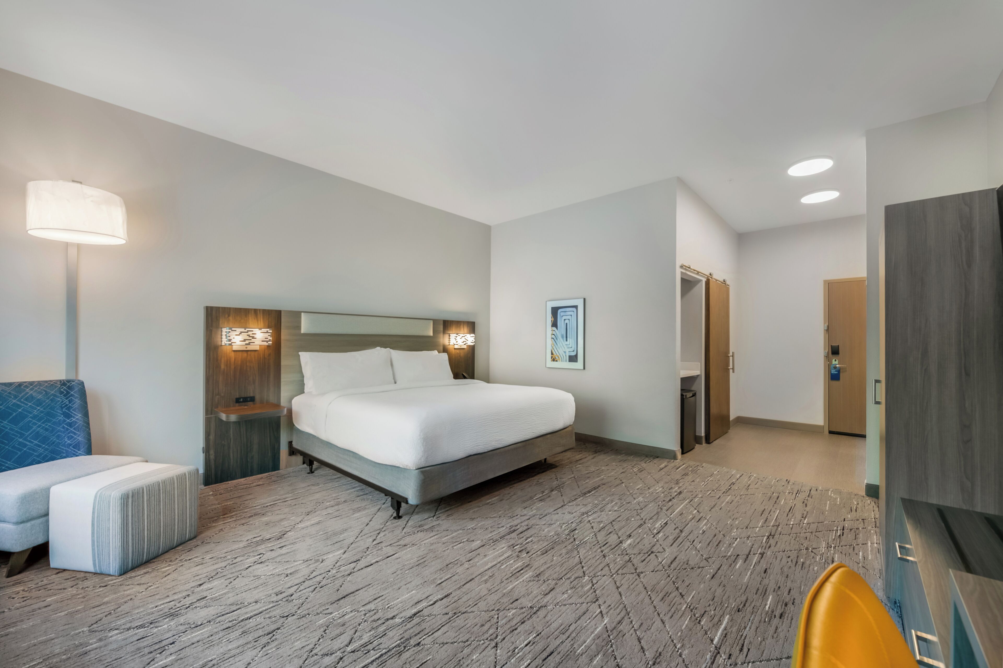 Habitació d'hotel amb llit, taules de nit, una làmpada, una cadira i un armari.
