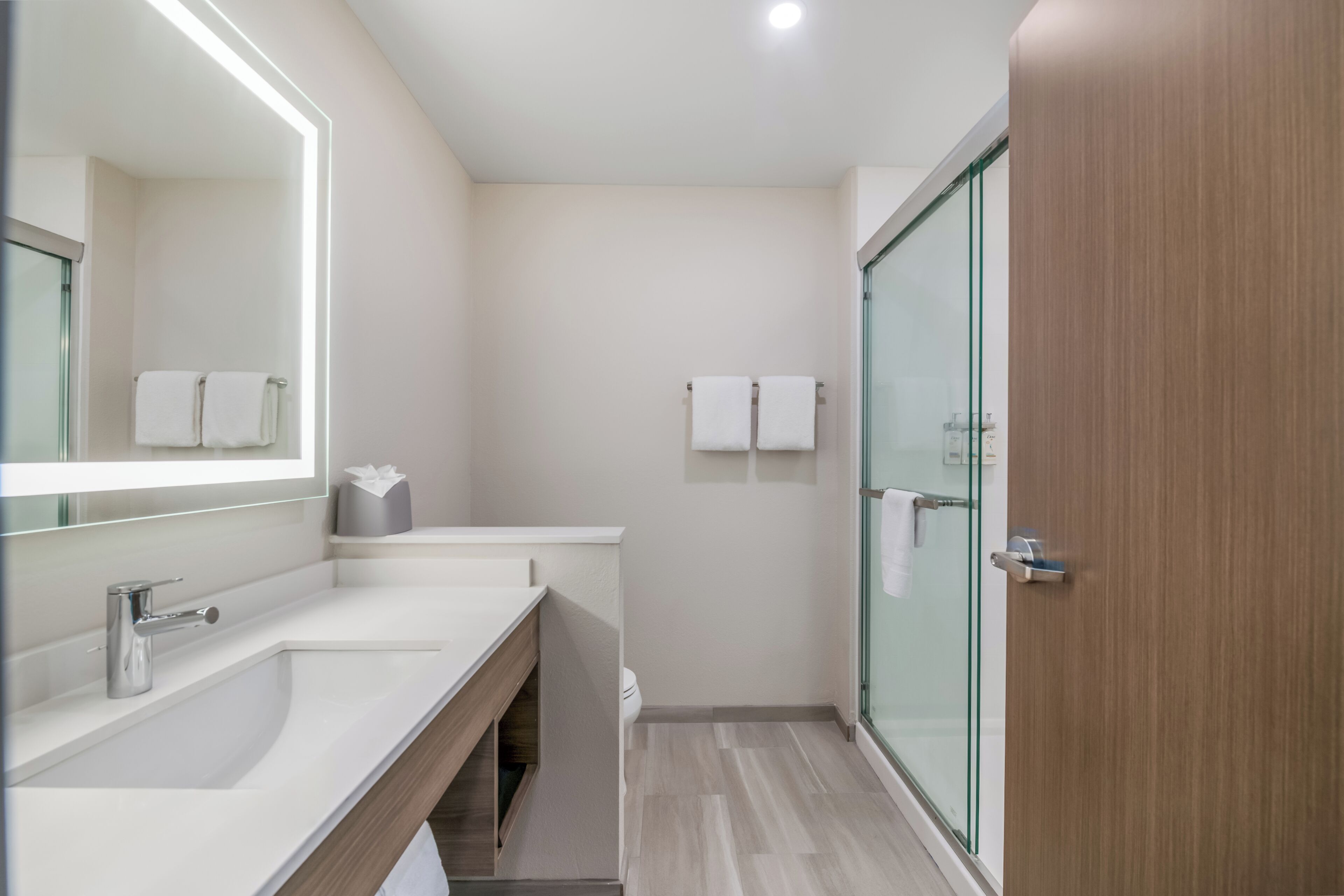 A modern bathroom with a large mirror, a sink, a toilet, and a glass shower enclosure.