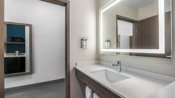 A modern bathroom with a large mirror, a sink, and a microwave on a shelf.