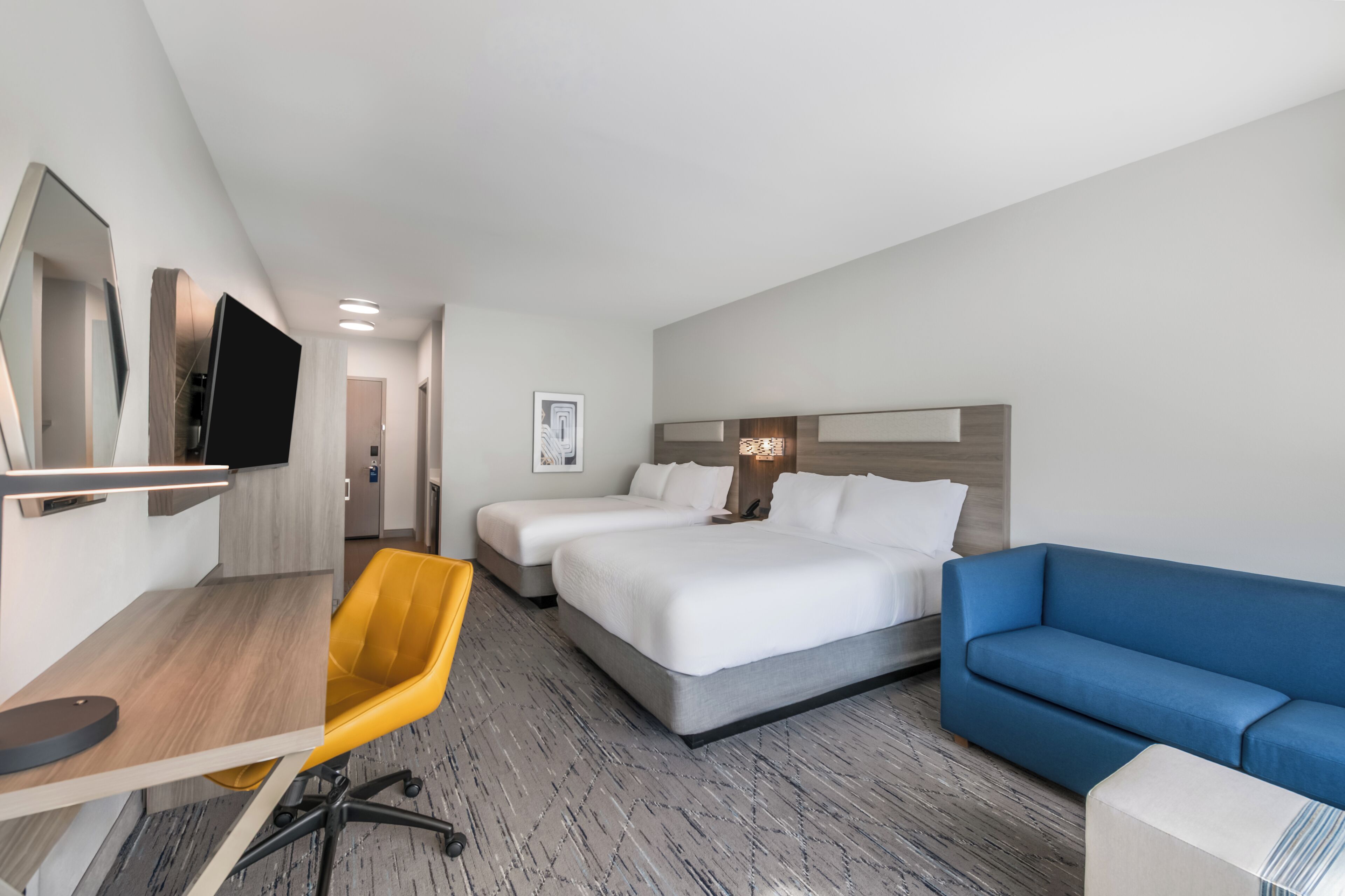 A hotel room with a desk, two beds, a blue sofa, and a television.